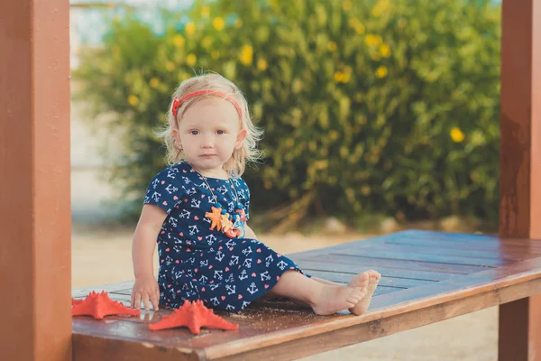 Bébé fille mignonne avec les cheveux blonds et la joue de pomme rose profiter des vacances d'été posant dans une belle plage pleine de sable portant une robe élégante — Photo