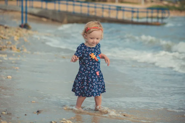 Ładna dziewczynka z blond włosy i różowy apple policzek wakacje lato czas pozowanie w pięknej plaży pełne piasku sobie stylowy sukienka — Zdjęcie stockowe