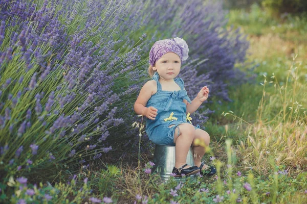 Fiatal szépség gyermek lány pózol central park rét levendula bokor viselt farmer ruha és a lila lila tarka selyemkendő misztikus barna szem — Stock Fotó