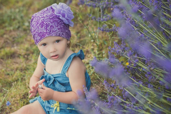 Menina de beleza jovem posando no prado do parque central perto do arbusto lavander vestindo vestido de jeans e bandana violeta roxa com olhos castanhos místicos — Fotografia de Stock