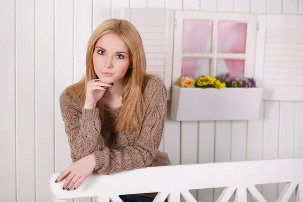 Amazing beautiful face lady girl with perfect skin and blond hairs posing on wooden bench in studio scenewearing french couture cosy wool sweater pullover