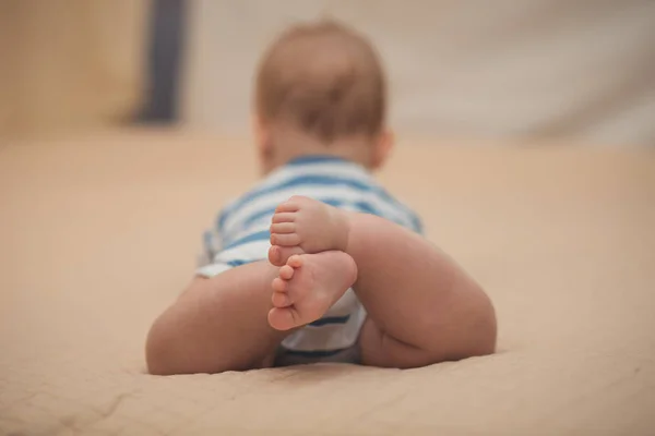 Nyfødt baby poserende på sofaen tæt blødt fokus på små ben fingre fra ryggen iført cool kropskjole - Stock-foto