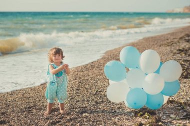 Sarı saçları ve kum plaj deniz tarafında sıradan çocuk giyim giymiş mavi beyaz balonlarla poz yaz saati tatil keyfini pembe elma yanak ile şirin kız bebek