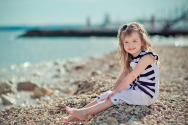 Şık giyinmiş sarışın çocuk kız zevk yaz tatili yalnız kameraya gülümseyen mutlu rahat parlak kıyafetleri genel şehir sahilde poz