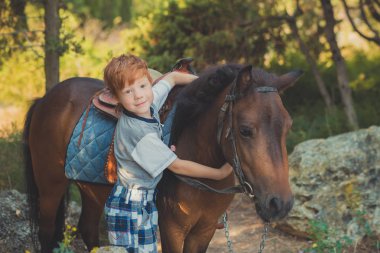 Handsome Young boy with red hair and blue eyes playing with his friend horse pony in forest.Huge love between kid shild and animal pet farm clipart