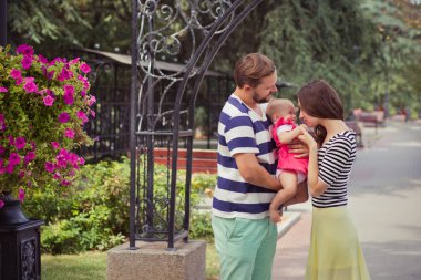 Baba Anne ve bebek genç ailesinin yürüyüş ve birbirine yakın buket çiçek ve ahşap Bank yaz şehir sokak Parkı üzerinde tutan çocuk kızı