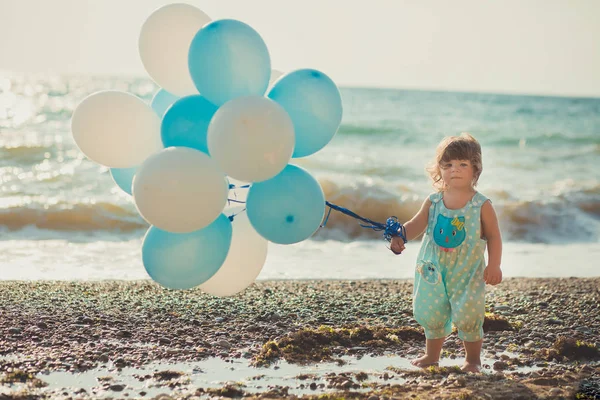 Schattig meisje met blond haar en roze apple Wang genieten van zomertijd vakantie poseren op zand strand zee kant met blauwe witte ballonnen dragen van casual kids kleding — Stockfoto