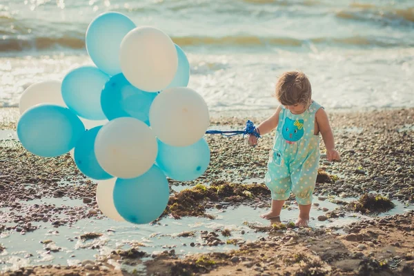 Schattig meisje met blond haar en roze apple Wang genieten van zomertijd vakantie poseren op zand strand zee kant met blauwe witte ballonnen dragen van casual kids kleding — Stockfoto