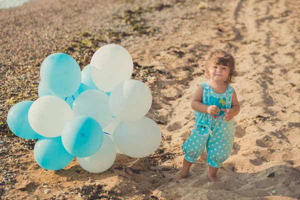 Schattig meisje met blond haar en roze apple Wang genieten van zomertijd vakantie poseren op zand strand zee kant met blauwe witte ballonnen dragen van casual kids kleding — Stockfoto