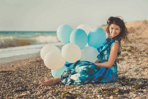 Increíble señora sensual mujer con pelos morenos y ojos azules hielo con globos blancos posando sentarse para la cámara en la playa de arena de verano con elegante vestido modish colorido descalzo — Foto de Stock