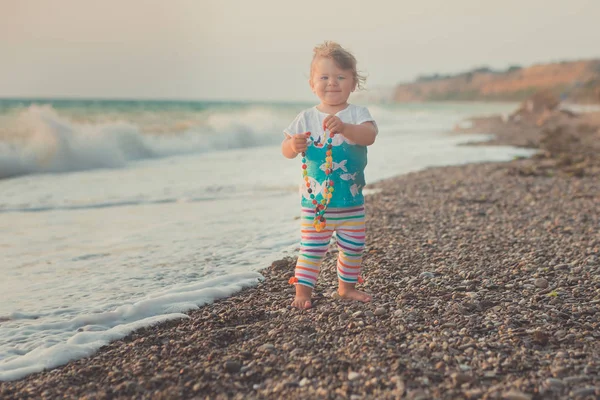Wonderbare droom foto van babymeisje met blonde haren, blauwe ogen en roze wangen poseren waarop zand strand zee kant retro oude stijl kleurrijke kleding dragen — Stockfoto