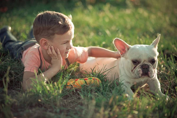 Szép jelenet közötti barátság szép fiú gyerek és a bika kutya kutyus pózol együtt a nyári a central parkban a friss zöld fű elegáns ruhában — Stock Fotó