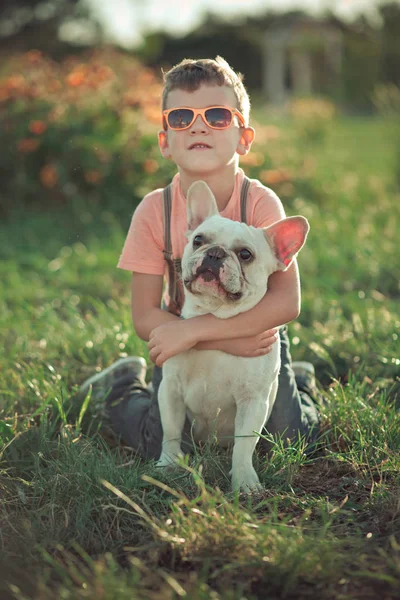 Scenă minunată de prietenie între băiețelul frumos și câinele taur pozând împreună în parcul central de vară pe iarbă verde proaspătă purtând haine elegante — Fotografie, imagine de stoc