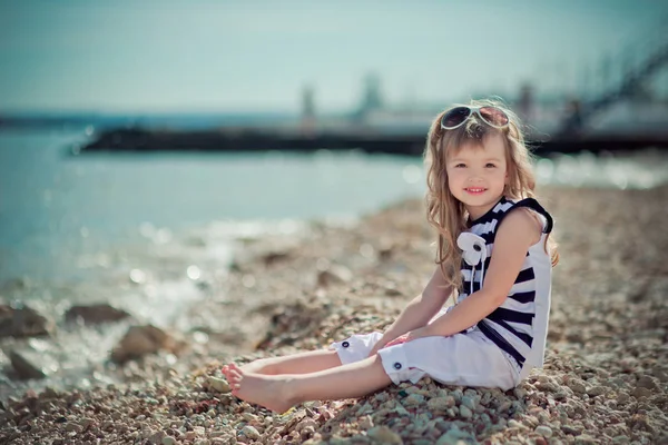Stijlvol geklede blonde kind meisje geniet van poseren zomervakantie op openbare stad strand dragen casual lichte kleding gelukkig lachend op de camera alleen — Stockfoto