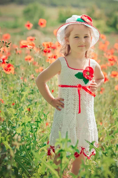 Aranyos szőke fiatal lány gyermek elegáns fehérbe öltözött kézzel akasztott ruhát visel tágas kalap felső pózol a rét, erdő mák mák Adoreable jelenet — Stock Fotó