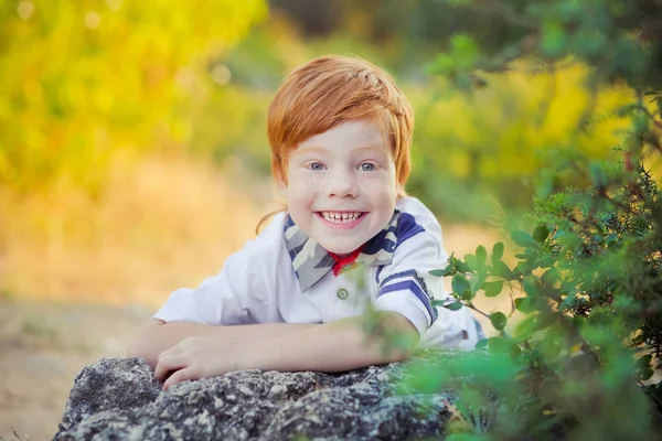 Schöner kleiner Junge mit roten Haaren und blauen Augen, der im Sommer auf der Waldwiese vor der Kamera steht und das warme Klima draußen in der Natur genießt — Stockfoto