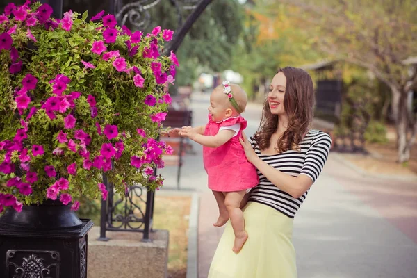 Fiatal hölgy barna anya zebra lágy inget és elefántcsont színű szoknyát boldog játszik a kislánya, a város utcáin parkban helyezkedik el a rózsaszín rózsa virágok nyári gyermek képe — Stock Fotó