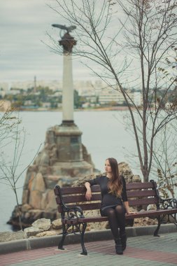 Güzel genç hamile hanımefendi kadın ile arka plan üzerinde şaşırtıcı anıt ahşap beanch waterfront sonbahar şehirde oturan esmer saç yalnız hayal ile