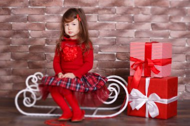 Genç esmer dolly Bayan kız şık kırmızı kazak kazak chequers onay ekose etek kayış ayakkabı olarak stüdyo kış kızak jumper pout dudak ve pembe yanakları ile poz oturan gülümseyen giyinmiş..