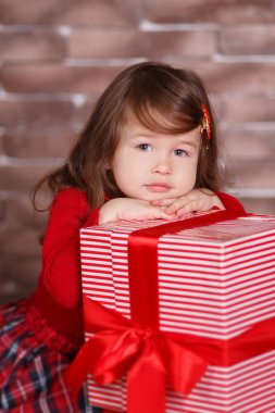 Kırmızı kazak kazak chequers onay ekose etek kayış ayakkabı pout dudak ve pembe yanakları ile büyük hediye ile stüdyo kış oturan poz gülümseyen genç esmer dolly Bayan kız şık giyinmiş.