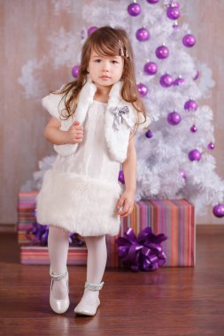 Beyaz elbise kürk ceket askısı ve stüdyo Kış Noel ağacı içinde poz gülümseyen ayakkabılar pout dudak ve pembe yanakları ile sunar rahat akşam resmi genç esmer dolly Bayan kız şık giyinmiş.