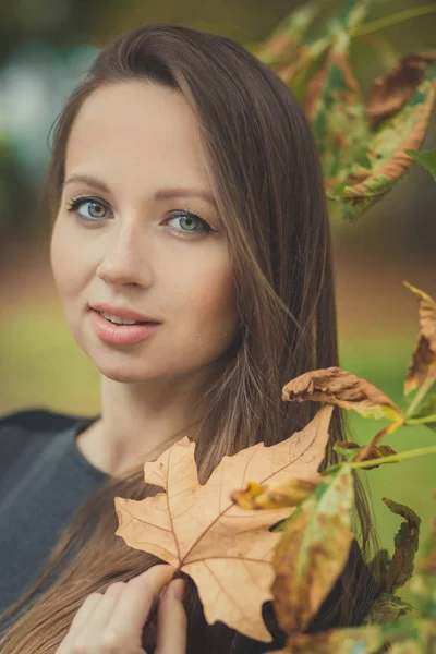 Adorable mujer linda dama con cabello moreno ojos verdes mejillas rosadas labios de la gota rosa y los dientes blancos posando para el retrato de la cámara con follaje de otoño — Foto de Stock