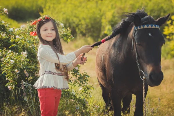 Mädchen mit brünetten Haaren und braunen Augen stilvoll gekleidet in rustikaler Dorfkleidung weißes Hemd und rote Hose am Gürtel posiert mit schwarzem jungen Pferd Pony — Stockfoto