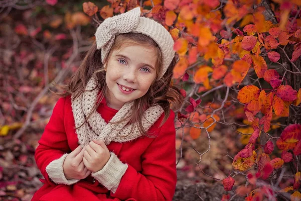 Schattig jong Russisch meisje stijlvol gekleed in warme rode handgemaakte jas blauw jeans laarzen en verslaafd hoofdband sjaal poseren in de herfst kleurrijk bos traject gezicht met freckling — Stockfoto