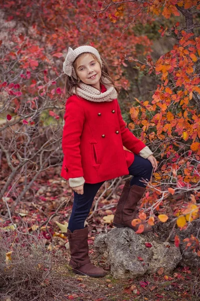 Schattig jong Russisch meisje stijlvol gekleed in warme rode handgemaakte jas blauw jeans laarzen en verslaafd hoofdband sjaal poseren in de herfst kleurrijk bos traject gezicht met freckling — Stockfoto