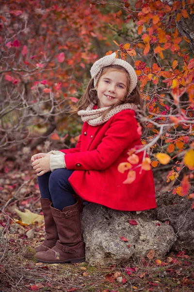 Schattig jong Russisch meisje stijlvol gekleed in warme rode handgemaakte jas blauw jeans laarzen en verslaafd hoofdband sjaal poseren in de herfst kleurrijk bos traject gezicht met freckling — Stockfoto