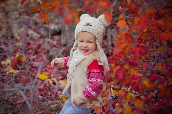 Roztomilá mladá Ruská dívka stylově oblečený do teplé bílé kožešiny ručně sako modré džíny bot a zahnutý čepice medvídek pózuje v podzimní barevné lesní stezka tvář s Růžové tváře — Stock fotografie