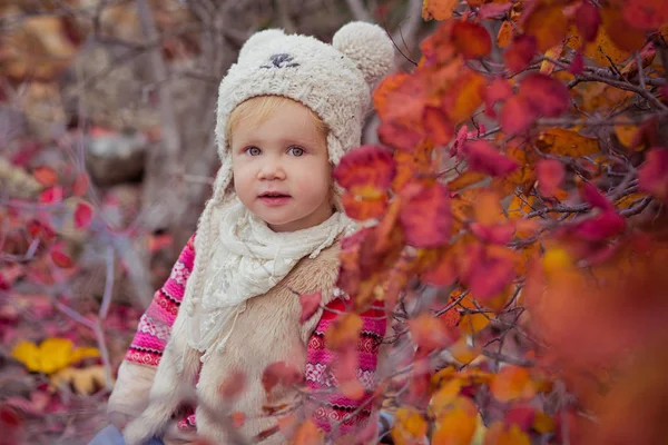 Bonito jovem russo bebê menina elegante vestido no quente branco pele artesanal casaco azul jeans botas e enganchado chapéu ursinho posando no outono colorido floresta caminho rosto com rosa bochecha — Fotografia de Stock