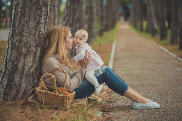 Boldog fiatal anya mam sylish öltözött jelentő baby lánya visel rózsaszín ruha szép kiadások életre együtt család ül az erdő-fa-és vadon termő bogyósok kosár — Stock Fotó