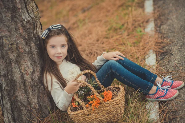 Симпатична молода дівчина з блакитними очима з м'яким волоссям і веснянкою щокою в білій сорочці і позує близько до старого дерева з дикими ягодами в кошику, дивлячись на камеру — стокове фото