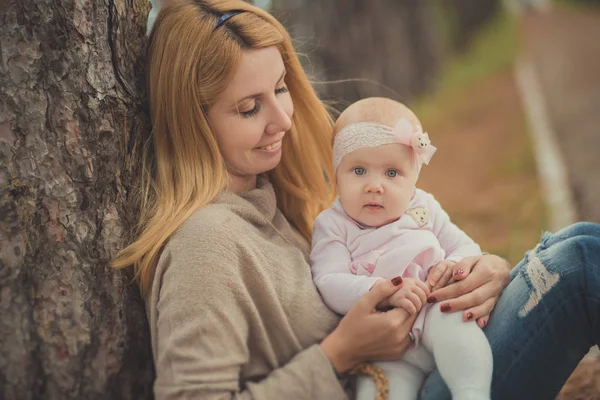 Glücklich junge Mutter mam sylish gekleidet posiert mit Baby-Tochter tragen rosa Kleid schöne Lebenszeit zusammen verbringen Familie sitzt im Wald in der Nähe von Baum und Korb mit Waldbeeren — Stockfoto