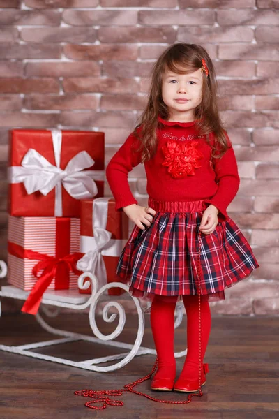 Jovem morena dolly menina elegante vestida com chequers de camisola pulôver vermelho verificar tartan saia alça sapatos sorrindo posando sentado em estúdio inverno trenó jumper com lábios de faneca e bochechas rosa . — Fotografia de Stock