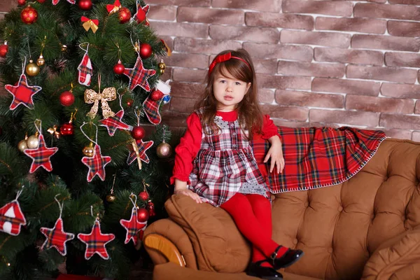 Jovem morena dolly senhora menina elegante vestida com chequers vestido vermelho verificar tartan saia alça sapatos sorrindo posando sentado no estúdio árvore de natal com lábios de faneca e bochechas rosa . — Fotografia de Stock