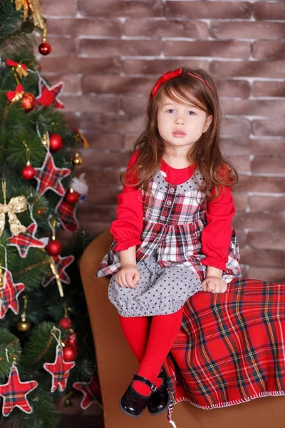 Jovem morena dolly senhora menina elegante vestida com chequers vestido vermelho verificar tartan saia alça sapatos sorrindo posando sentado no estúdio árvore de natal com lábios de faneca e bochechas rosa . — Fotografia de Stock