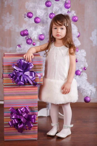 Jovem morena boneca menina elegante vestida de noite acolhedora vestido branco oficial sapatos de pulseira de casaco de pele sorrindo posando em estúdio inverno árvore de natal e presentes com lábios de faneca e bochechas rosa . — Fotografia de Stock