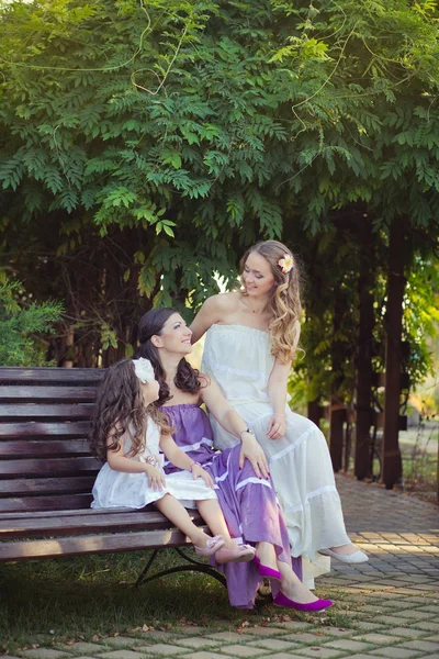 Adoring Brunette blond chestnut blue eyes sisters girls wearing cosy night white purple dress enjoying lifetime together summer sunny day in garden forest posing wooden bench happy smiling — Stock Photo, Image
