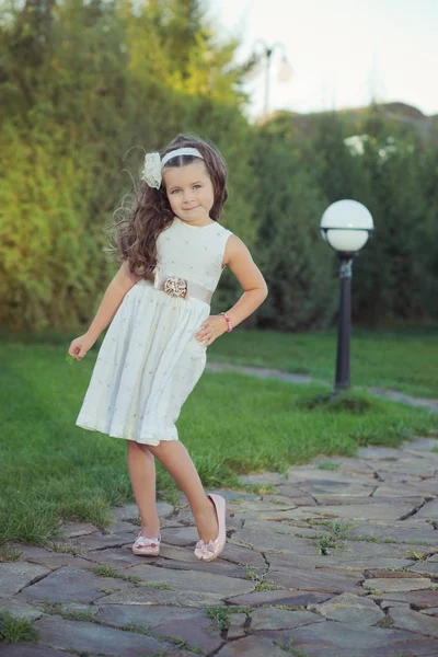 Chica joven castaña en vestido elegante noche blanca posando cerca de la lámpara del parque sonriendo y disfrutando de vacaciones fin de semana domingo verano primavera día soleado en el jardín de hierba verde — Foto de Stock