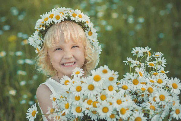 Aranyos fiatal szőke lány fehér szellős ruhában pózol a daisy Kamilla rét, csokor virágot keze basket fém vödör és a koszorú anademon felső fej mosolyogva. — Stock Fotó