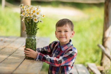 Sevimli fermer yakışıklı çocuk kovboy kot pantolon deri inek şapka happyly gülümseyerek çiçeklerle köy yaşamı günde yaz zevk.