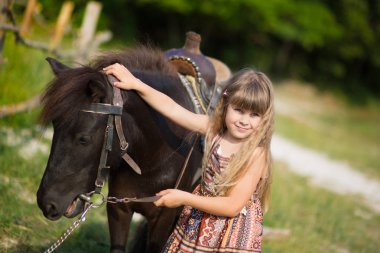 Sevimli fermer güzel kız kovboy happyly gülümseyerek ve atın üzerinde oturanbir deri inek şapka giyen çiçekli köy yaşamı günde yaz zevk kot pantolon .
