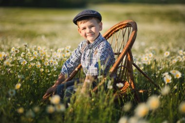 Kot pantolon ve çayır chamomiles daisy, tahta sandalyede oturan ve zevk yaz günü vallage grupta gülümseyen forması giyen sevimli yakışıklı çocuk.