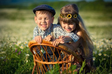 Kot pantolon ve güzel kız chamomiles papatya çayır üzerinde birlikte ahşap sandalye üzerinde oyun ve zevk yaz günü vallage grupta gülümseyen gömlek sittingand giyen sevimli yakışıklı çocuk.