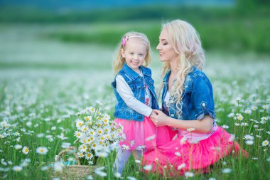 Anne ve kızı bir piknik papatya alanındaki tarih. Kot ceket ve pembe giyen iki güzel sarışın anne etek ve küçük kız papatya alanında bulunan buket dandalion sepet kucaklayan