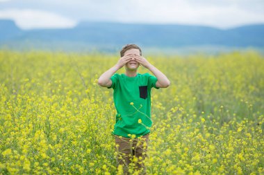 Mutlu sevimli yakışıklı çocuk çocuğun yeşil çim çim sarı çiçek açan ile karahindiba çiçekler güneşli bahar ya da yaz günü. Rüya ve bir buket toplama rahatlatıcı küçük çocuk