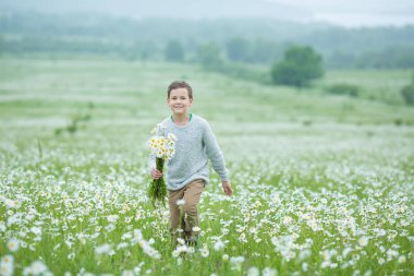 Rain and sunshine with a smiling boy holding an umbrella and running through a meadow of wildflowers dundelions chamomile daisy and holding bouquet stylish dressed in white sweeter clipart