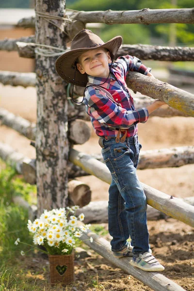 Niedlichen Fermer gutaussehenden Jungen Cowboy in Jeans genießen Sommertag im Dorfleben mit Blumen tragen ledernen Kuhhut glücklich lächelnd. — Stockfoto